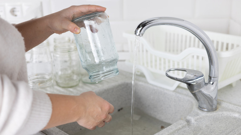 A woman cleaning the labels off a glass jar