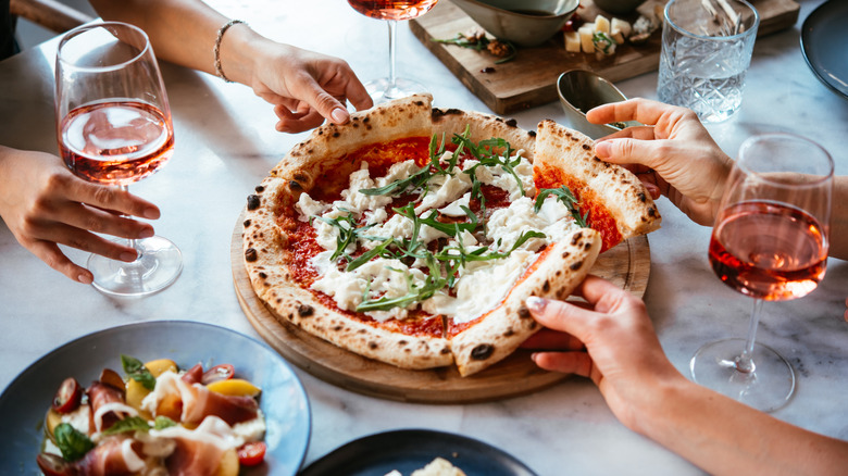 Hands grabbing a pizza
