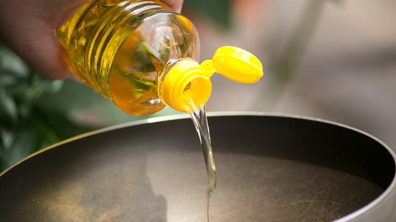 Cooking oil in a plastic yellow bottle being poured into a pan