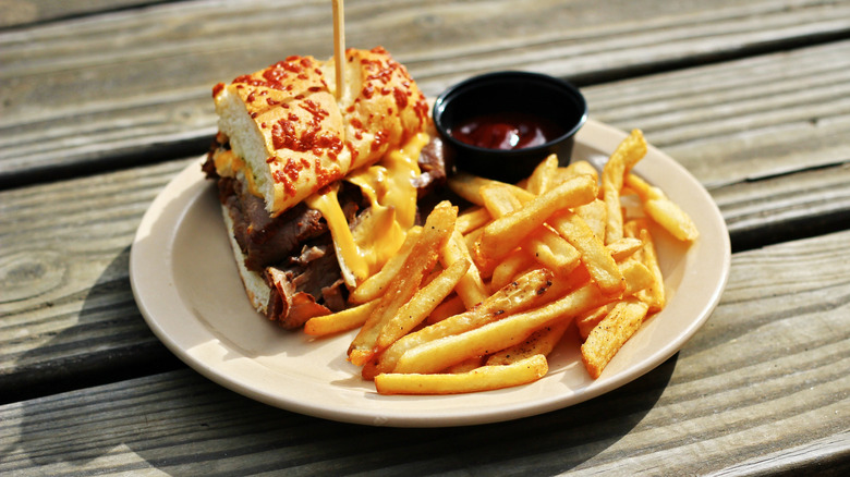 Burger with cheese and fries on a white plate on a wooden table