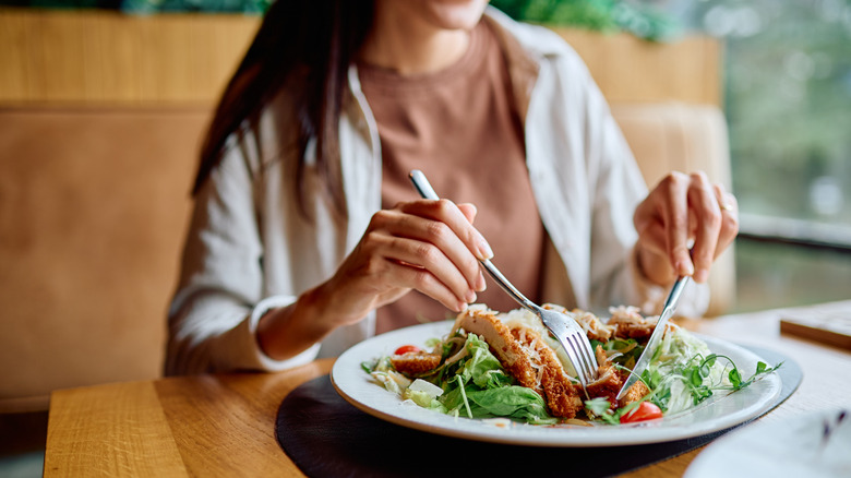 A solo diner eating salad with a fork and a knife.
