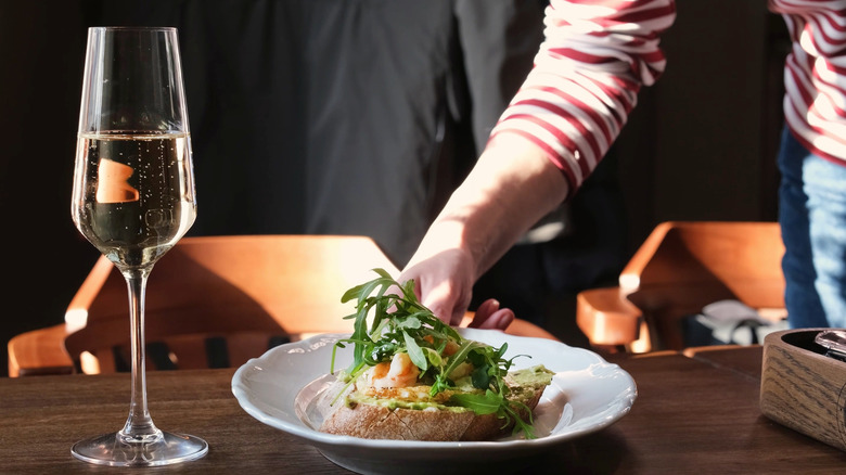 A hand serving a single dish on the table with a bubbly drink.