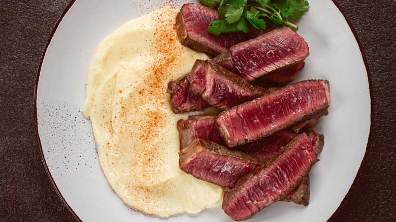 Top-down view of steak and seasoned mashed potatoes on a white plate