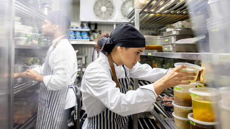 A line cook placing containers of food in a commercial walk-in cooler.