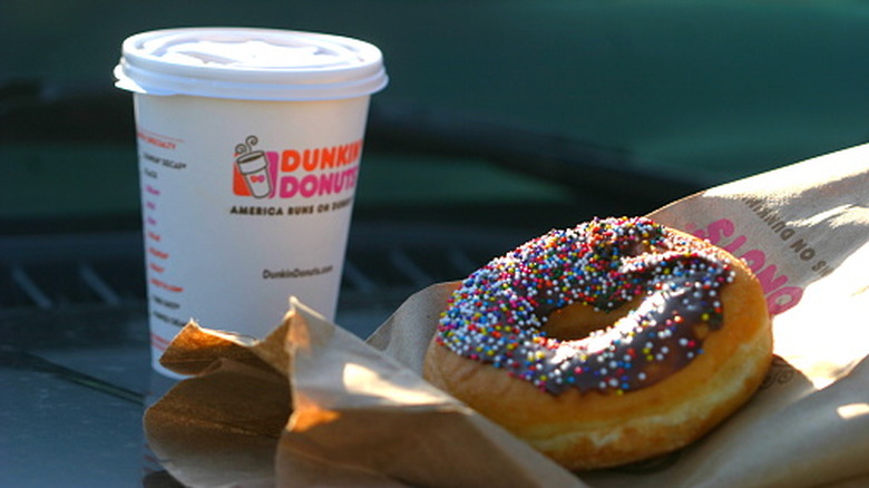 Dunkin' to-go coffee next to a donut with chocolate frosting and rainbow sprinkles