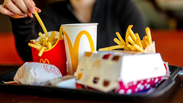 Person enjoying McDonald's fries off a tray of food with burger boxes and a drink