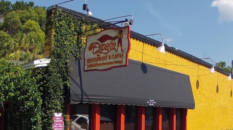 The exterior of the restaurant with a yellow wall, black awning, and sign with the name