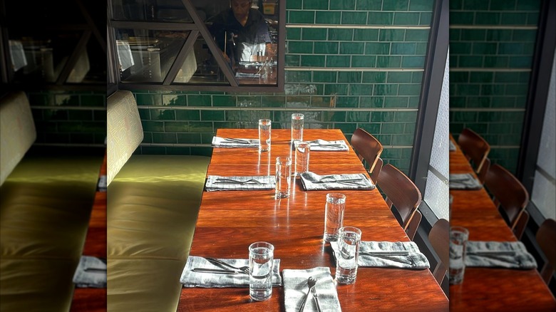 A wooden table with place settings in front of a green tile wall