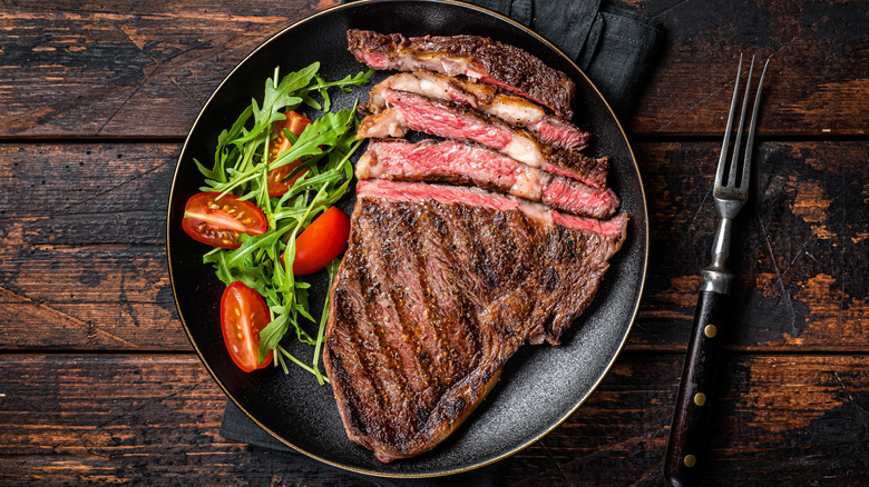Grilled, sliced ribeye steak with salad on black plate