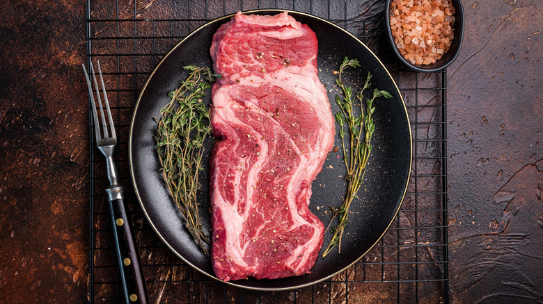 Raw chuck eye steak on cutting board with herbs and seasonings