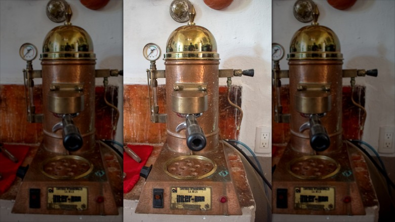 An old espresso machine on a worn looking counter