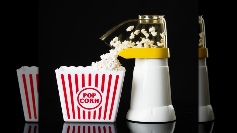 A countertop popcorn maker popping popcorn into a large bowl with a black background