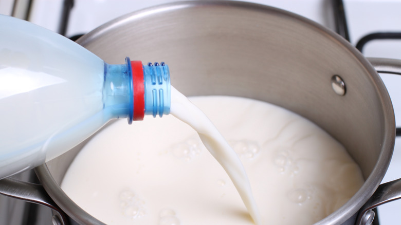 Milk being poured from a bottle into a saucepan on a stove.