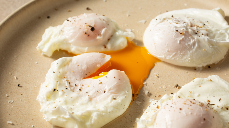 A plate of poached eggs with one halfway open and yoke spilling out.