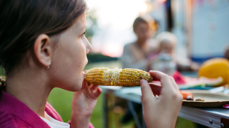 A girl eating a slightly charred corn cob, with the middle partially eaten
