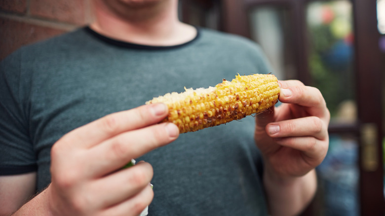 A person holding a halfway eaten corn cob