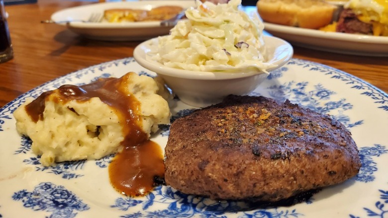 Cracker Barrel hamburger steak on a plate with mashed potatoes and cole slaw in a tiny dish on the table.