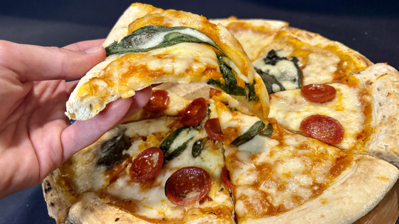 hand holding pizza slice over full pizza