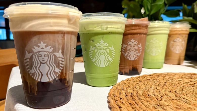 A lineup of 5 new Starbucks protein drinks, with a plain cold foam with cold brew, vanilla protein latte, protein matcha latte, chocolate cold foam, and matcha cold foam
