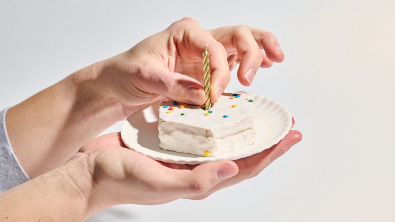 Hand placing a candle into a birthday cake on a plate.