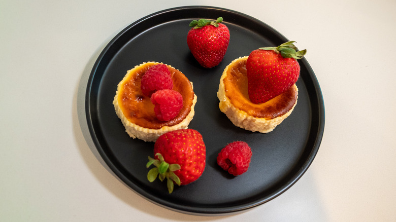 Two Trader Joe's Basque-style Cheesecakes with strawberries and raspberries on a black plate on a white background