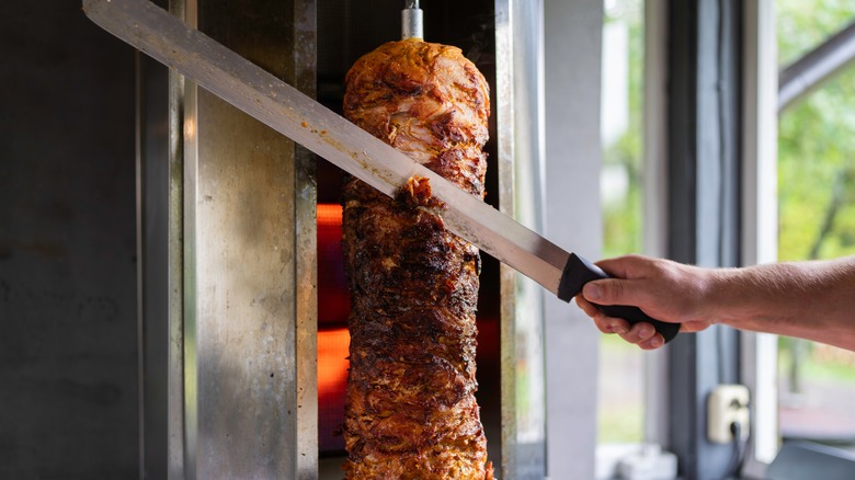 A traditional Döner kebab with someone slicing off a piece using a long knife