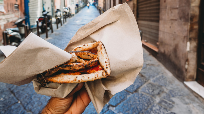 Pov view of a man eating a typical "Pizza a portafoglio" in Naples, Italy.