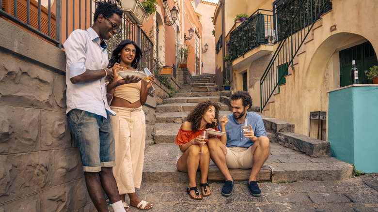 A group of people sitting on old stone steps while eating plates of pasta.