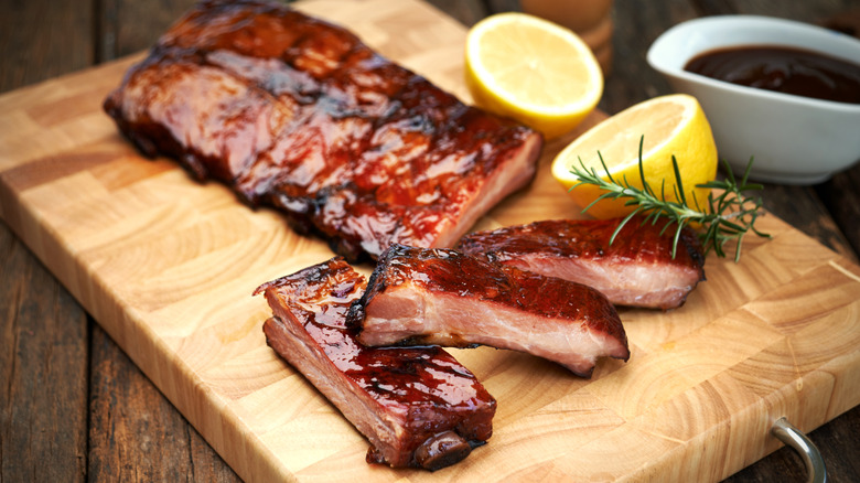 Pork ribs rest on a wooden cutting board with lemons and herbs