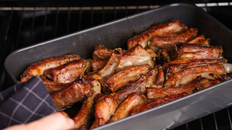 Person taking out a tray of pork ribs from the oven