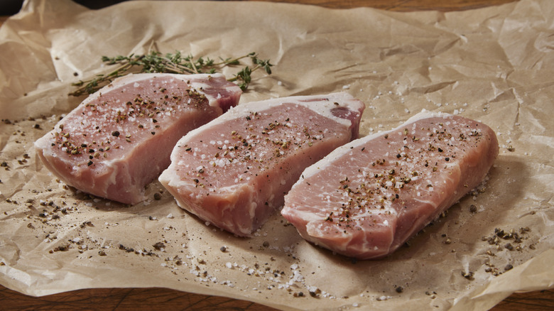 Pork chops on parchment paper with herbs, salt, and pepper