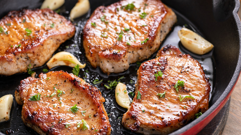 Four juicy, pan-seared, oven-finished pork chops with garlic sit in a cast-iron skillet.