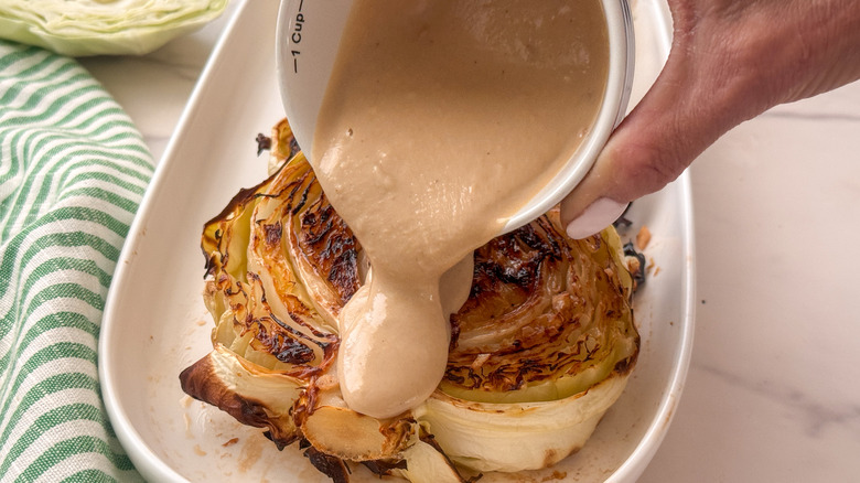 hand drizzling tahini sauce over cabbage
