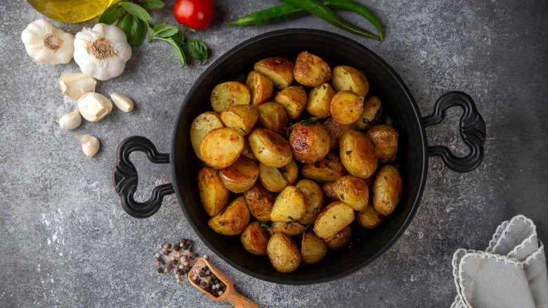 A batch of golden roasted potatoes is photographed from above, herbs and aromatics on the side.