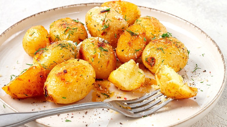 Roasted baby gold potatoes with grated parmesan cheese and fresh dill on a cream-colored plate.