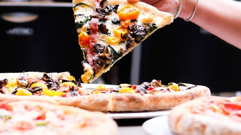 Person picking up a slice of pizza surrounded by more pies