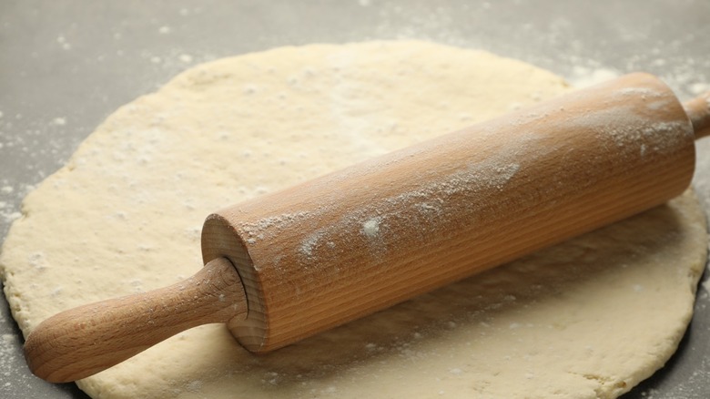 Wooden rolling pin covered with flour resting on dough