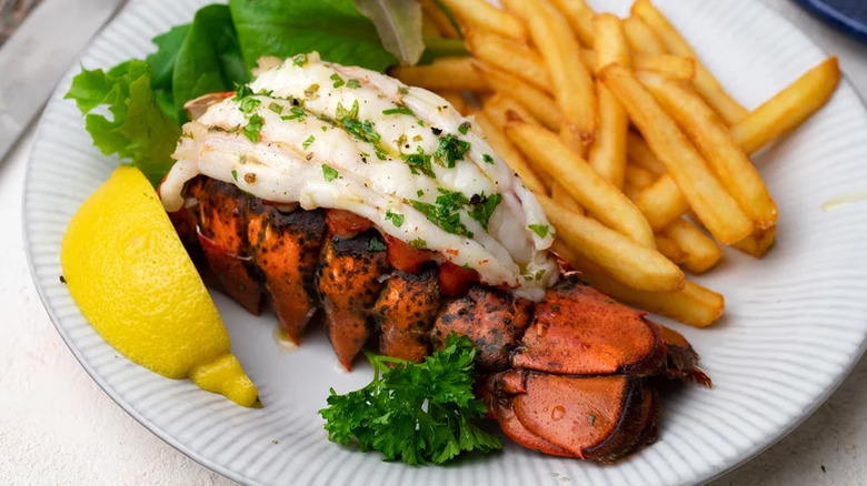 Lobster tails on a plate with fries and a lemon wedge.