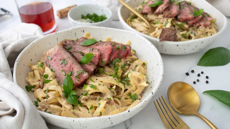 Steak Alfredo dish with herbs on a table with cutlery and drinks.