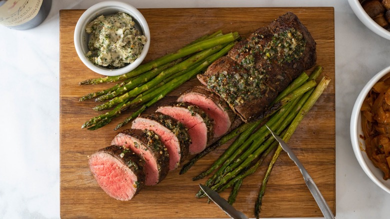 Chateaubriand on a cutting board with tongs.