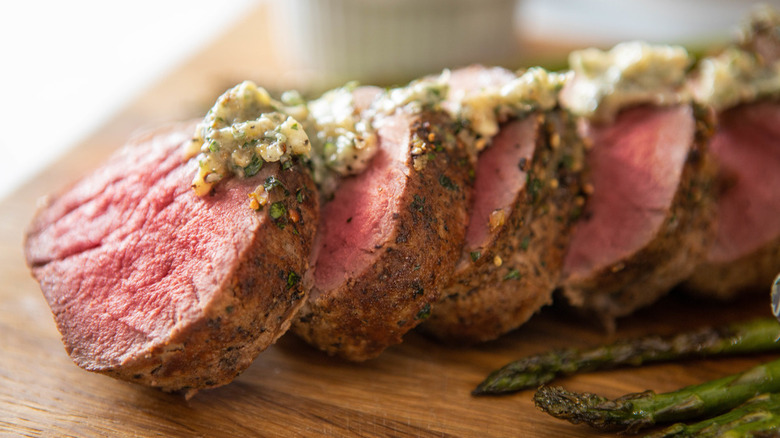 Roast beef with sauce and asparagus on cutting board.