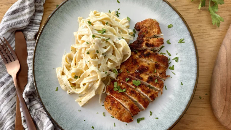 Chicken Alfredo on a plate next to cutlery.