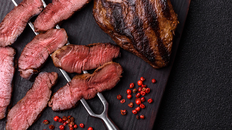 Slices of steak on a cutting board, some pierced with a fork skewer