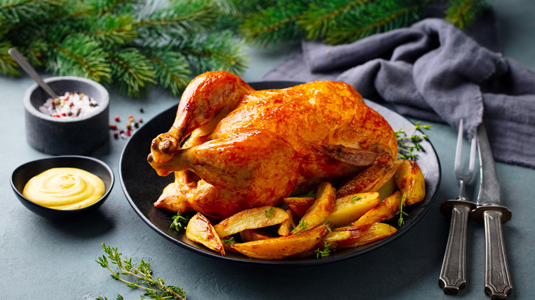 Roasted chicken on a black plate with potato wedges