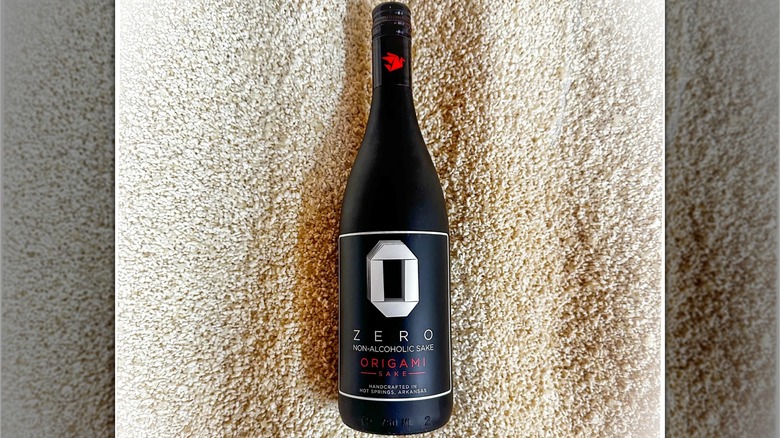 Black bottle of Origami Non-Alcoholic Sake on a bed of what looks like sawdust