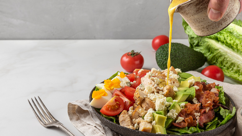 Dressing is poured over a Cobb salad.