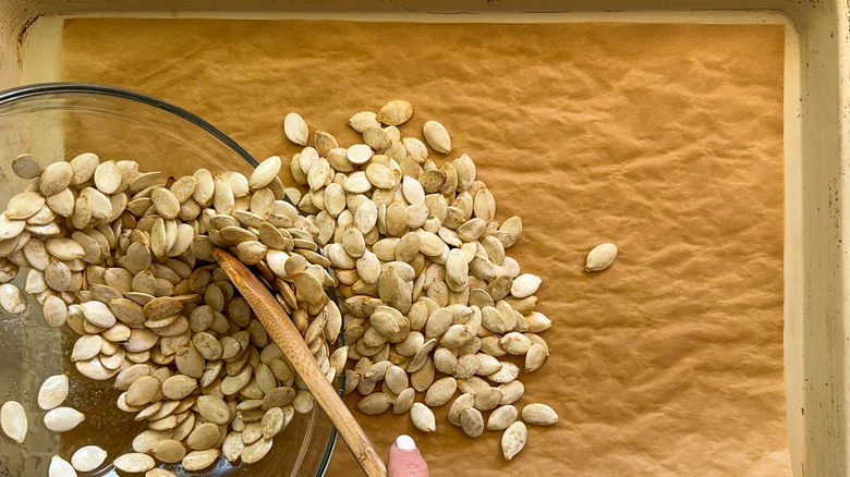 adding pumpkin seeds to baking sheet