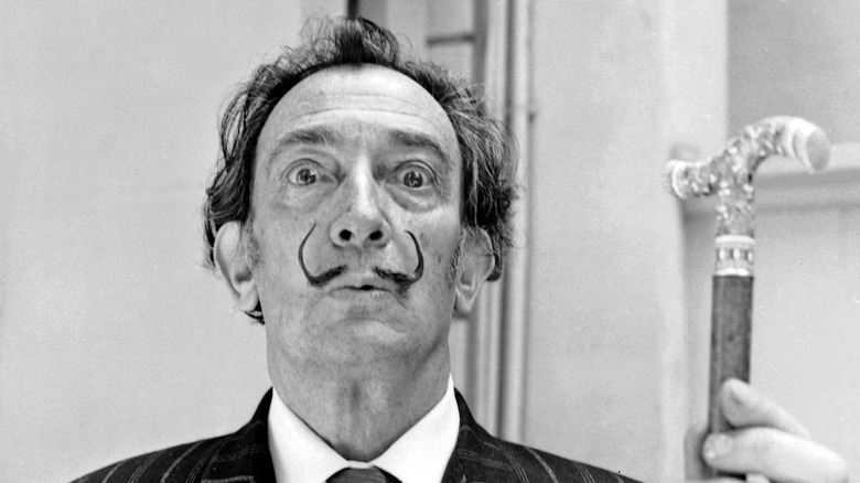 Salvador Dali with his signature mustache holding a cane with an elaborate handle