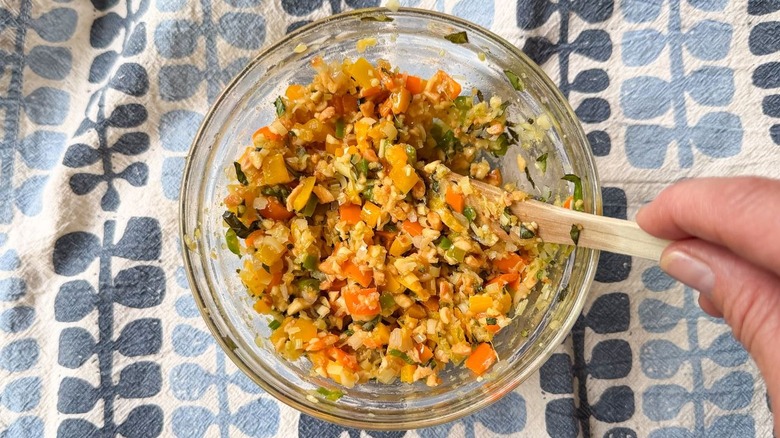 Stirring crushed peanuts and basil in to sambal in glass bowl