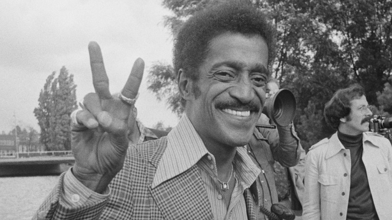 Sammy Davis Jr. smiling and holding up a peace sign